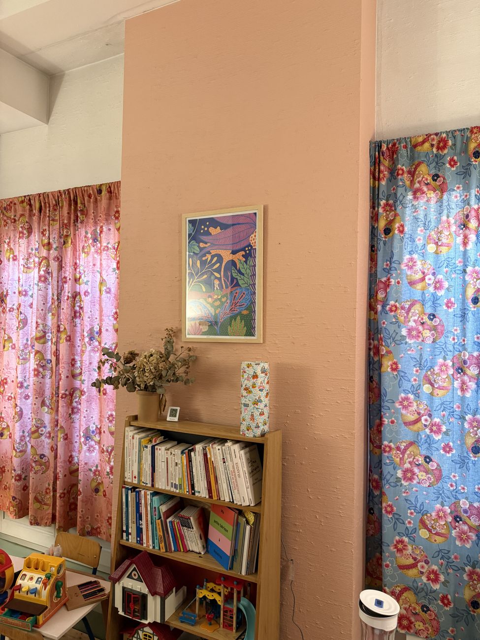 Mur rose, bibliothèque et rideaux fleuris.